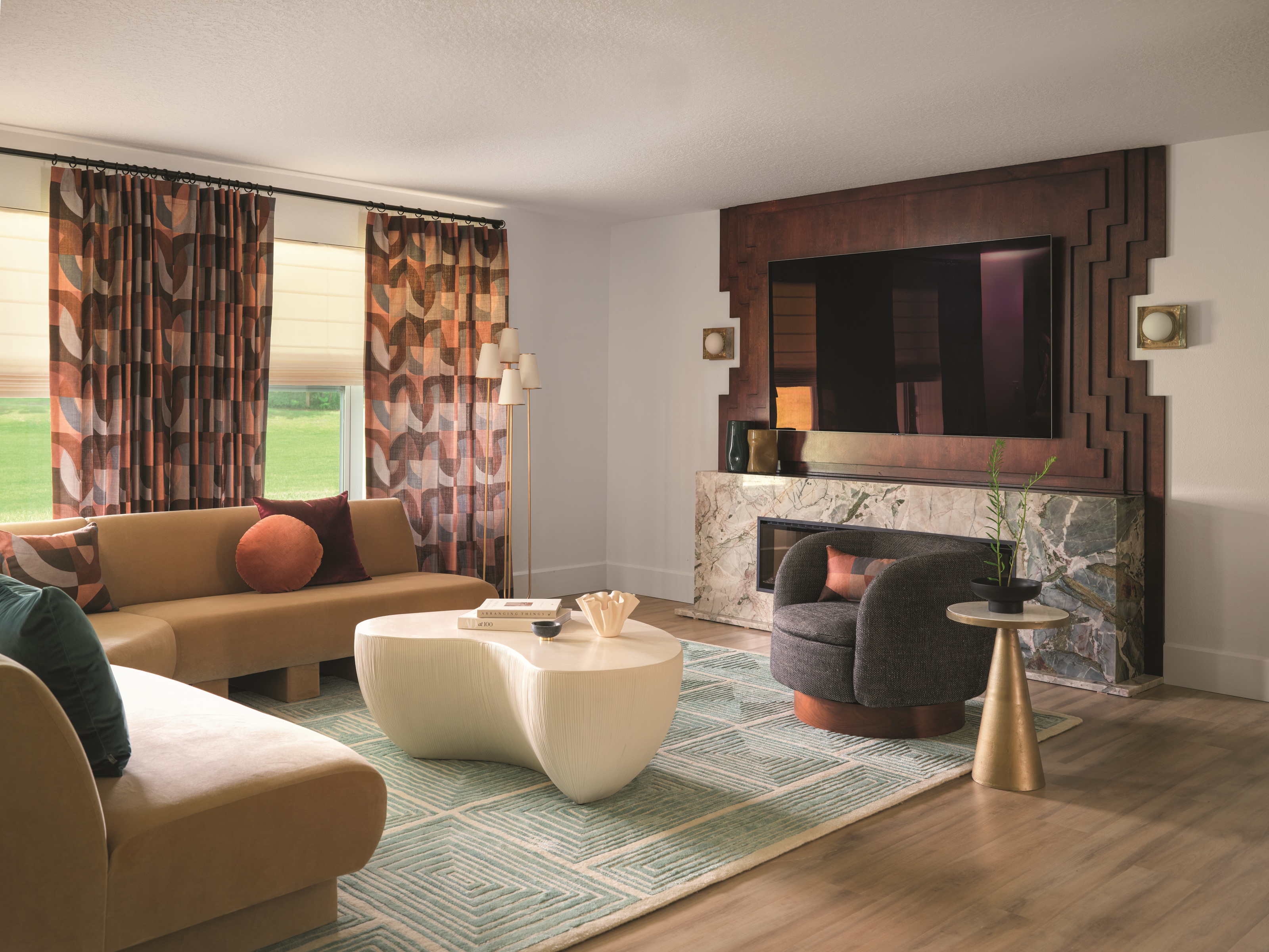 a living room with a wood tv wall, marble fireplace and patterned curtains, with a beige corner sofa