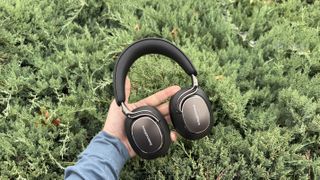 Bowers & Wilkins Px8 S2 headphones in black being held in front of a green bush