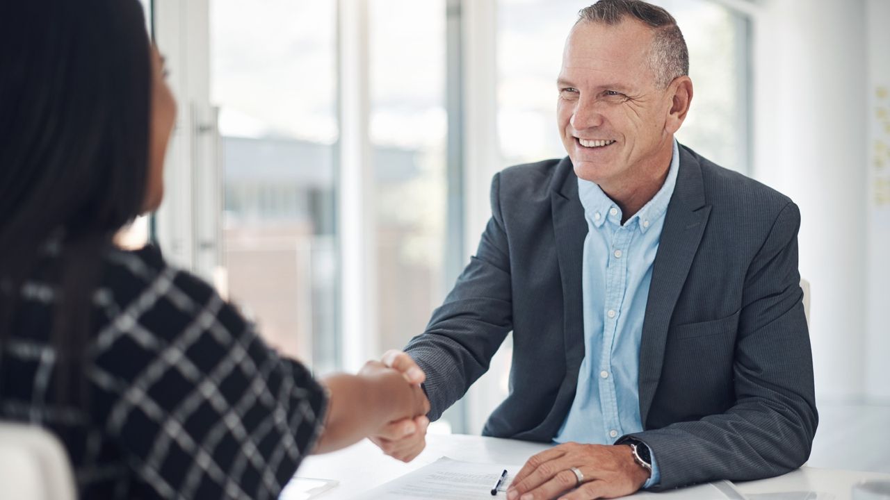 Photo of a man shaking hands with someone behind a desk after doing business in a modern office