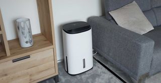 Large dehumidifier in a gray living room to support an article on w&h asking how does a dehumidifier work