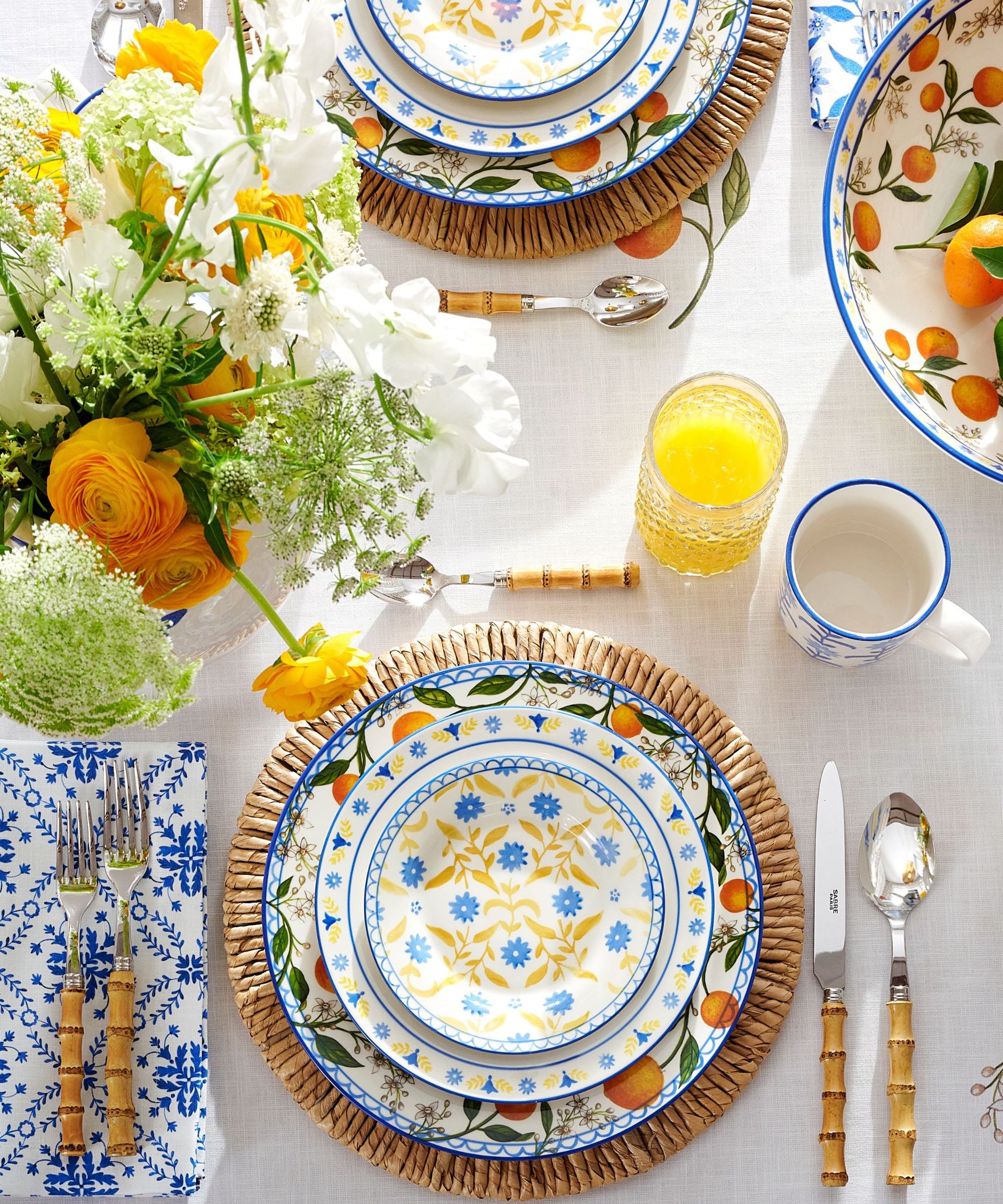 tablescape from the Mark D Sikes x Pottery Barn collaboration with blue and white patterned tableware, rattan placemats, bamboo flatware and orange citrus motifs