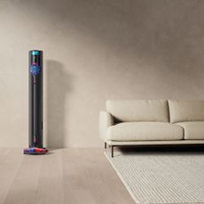 Dyson V10 Konical sitting on its dock in a minimal living room next to a white sofa