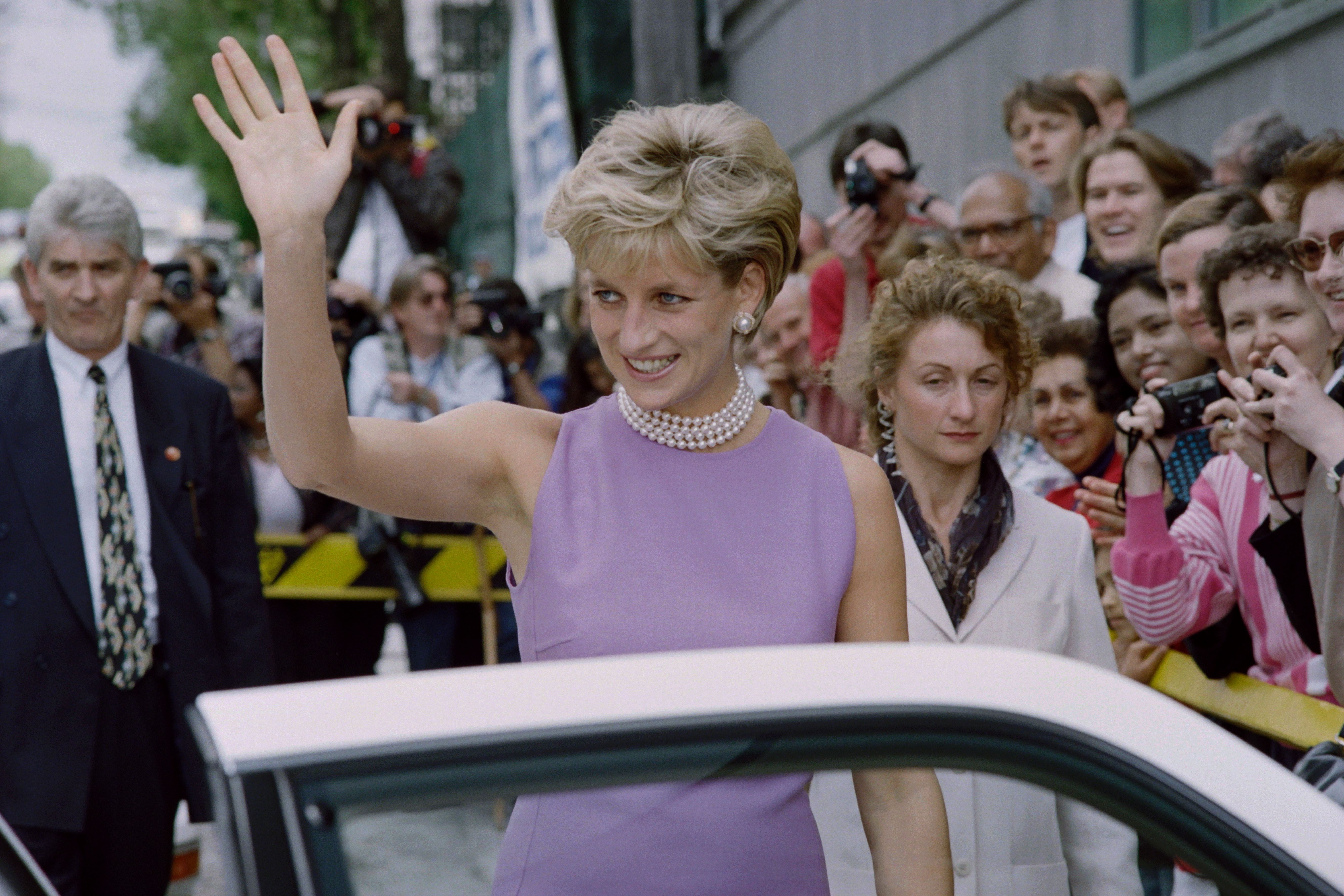 Princess Diana wearing a purple dress and pearls waving to a crowd in 1996