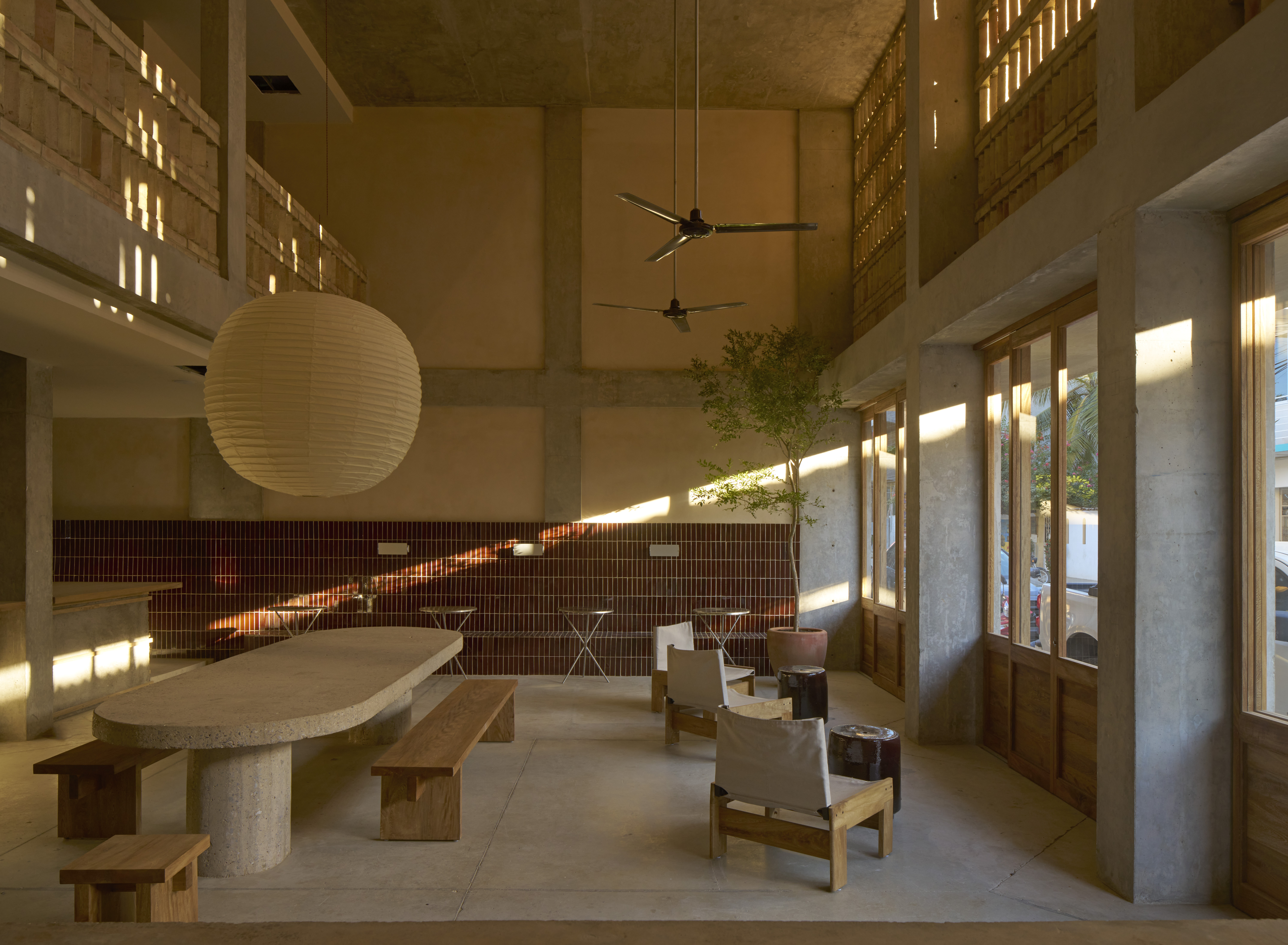 A Mexican brutalist retreat pairs cement walls with wood furnishings in creamy tones, paper lanterns, and chrome ceiling fans.