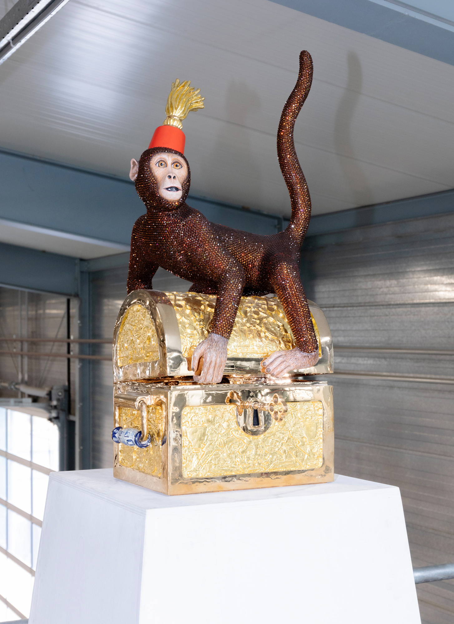 A sculpture of a diamond-encrusted monkey wearing a red hat and sitting on a golden treasure chest inside Studio Job&#039;s Tilburg workshop