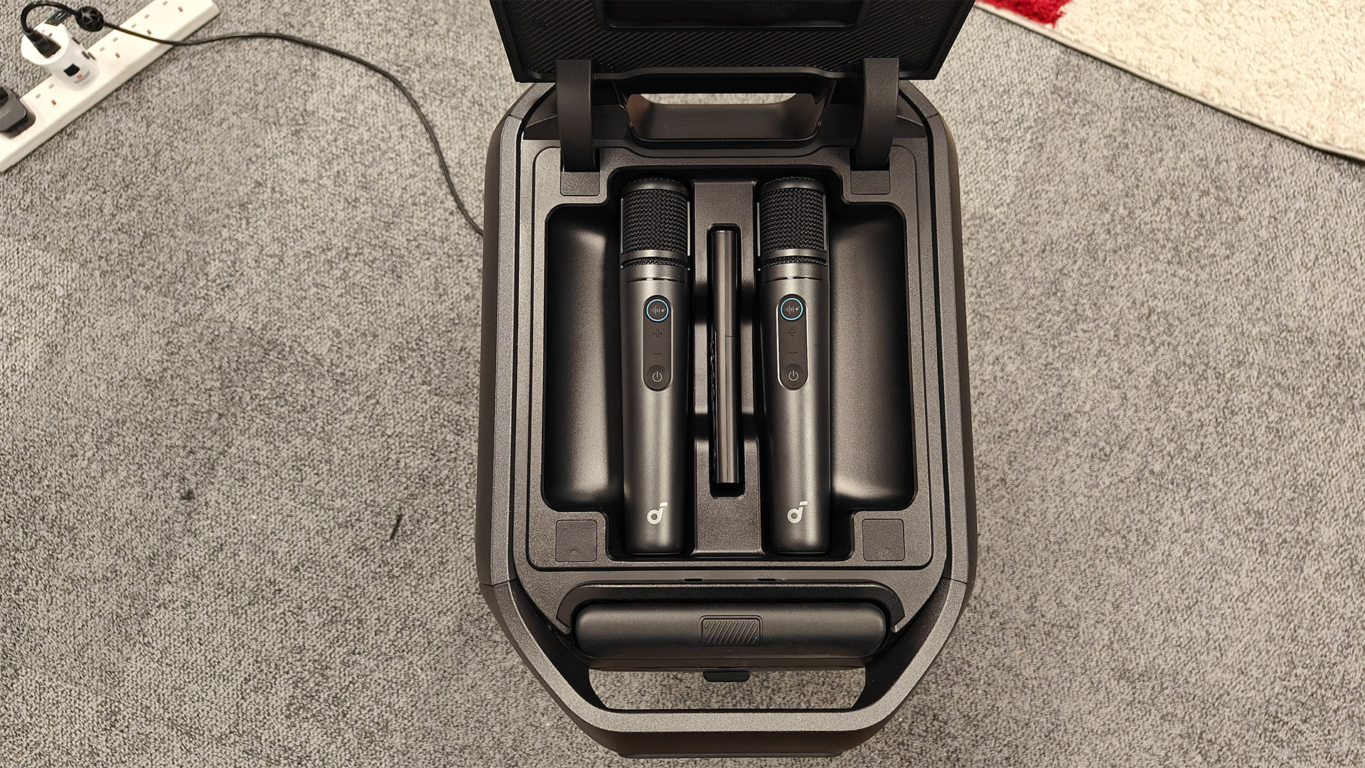 Soundcore Nebula X1 Pro home cinema projector on grey carpet, top of unit is open showing microphone storage