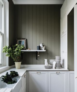 kitchen with white cabinets and dark green panelled wall with decorative shelf