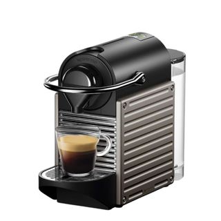 A silver and black Nespresso Pixie coffee maker with a coffee cup on it