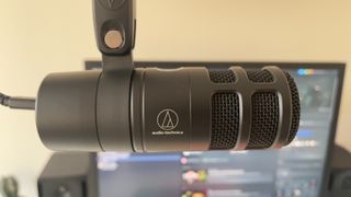 The Audio-Technica AT2040USB microphone on a mic stand in front of a monitor