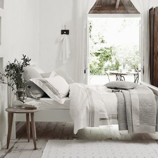 all-white and gray bedroom with white bed linen, and wide open doors onto garden
