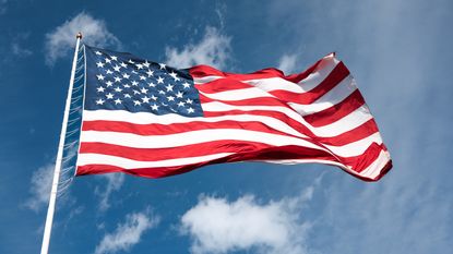 The American flag blowing in the wind against a blue sky.
