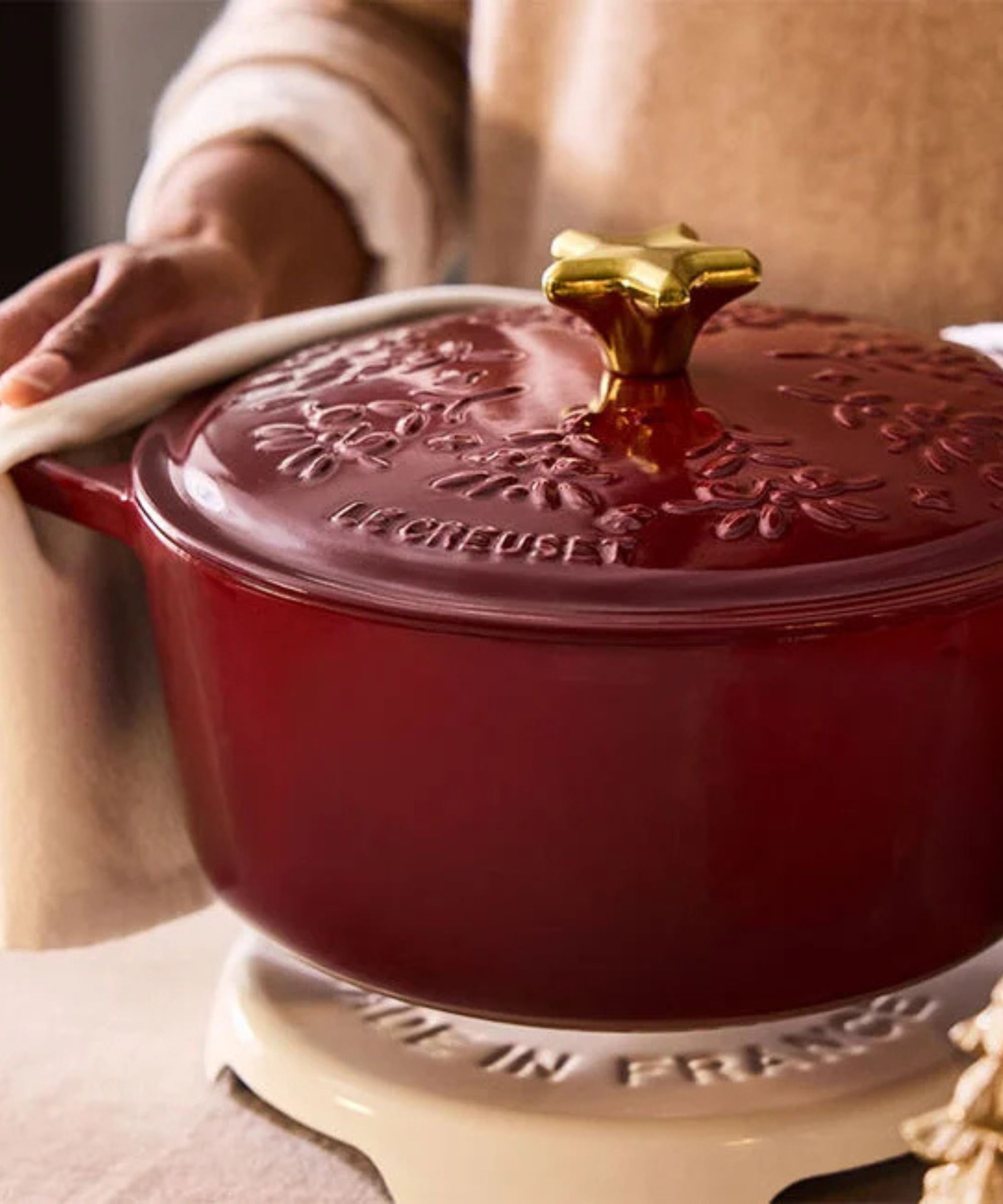 A deep red Dutch oven with holly embossed on the lid, with a gold star shaped lid handle.