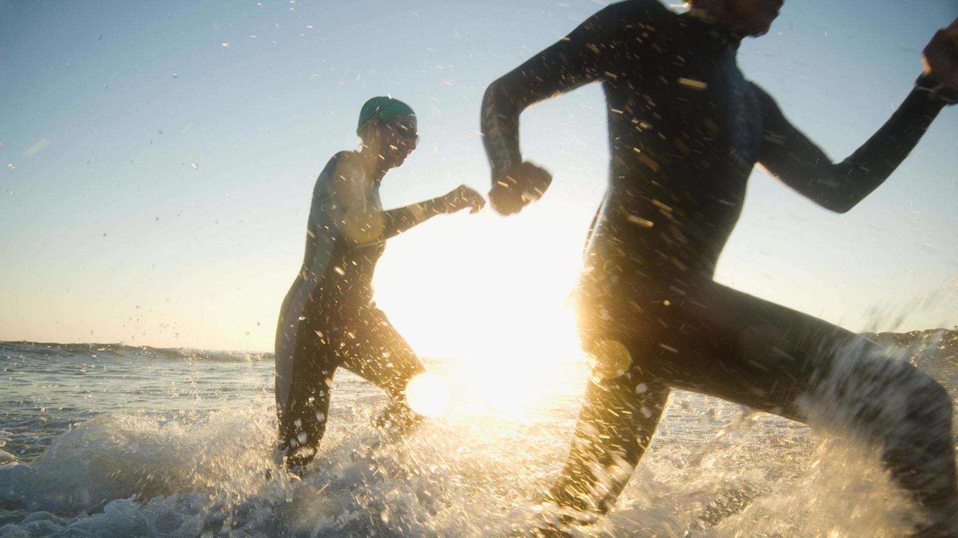 Swimmers running in the surf and waves in wetsuits with sun shining down