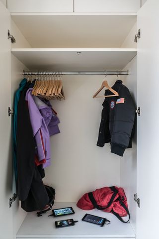 A wardrobe cupboard with three coats, a dozen wooden hangers and three mobile phones.