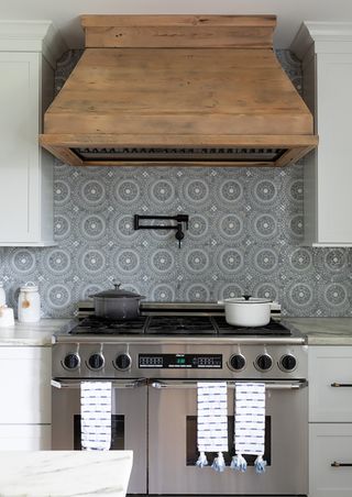 kitchen with wooden cooker hood blue and white patterned tiles and stainless steel oven with pot filler