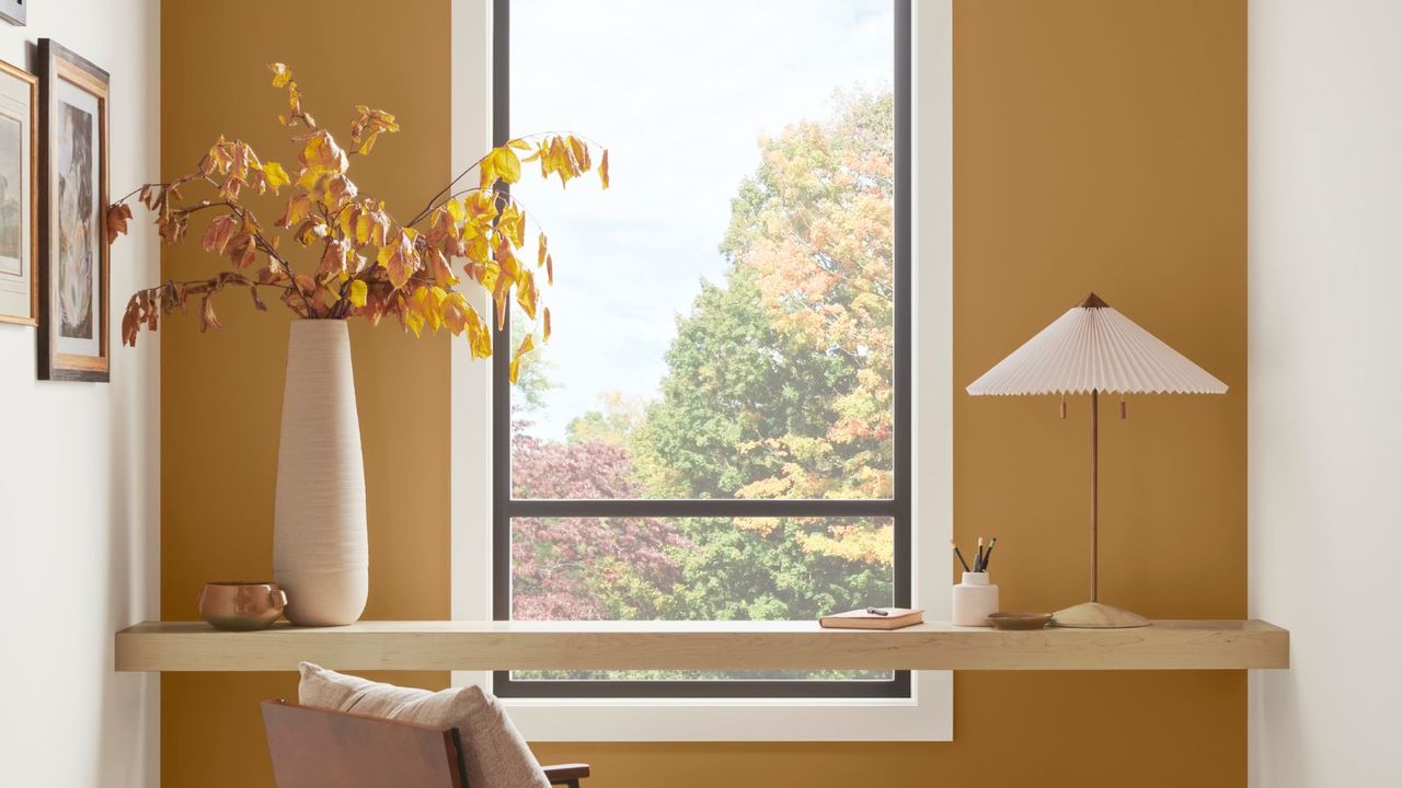 corner of home office with dark yellow wall with wooden desk in front of large window overlooking landscape