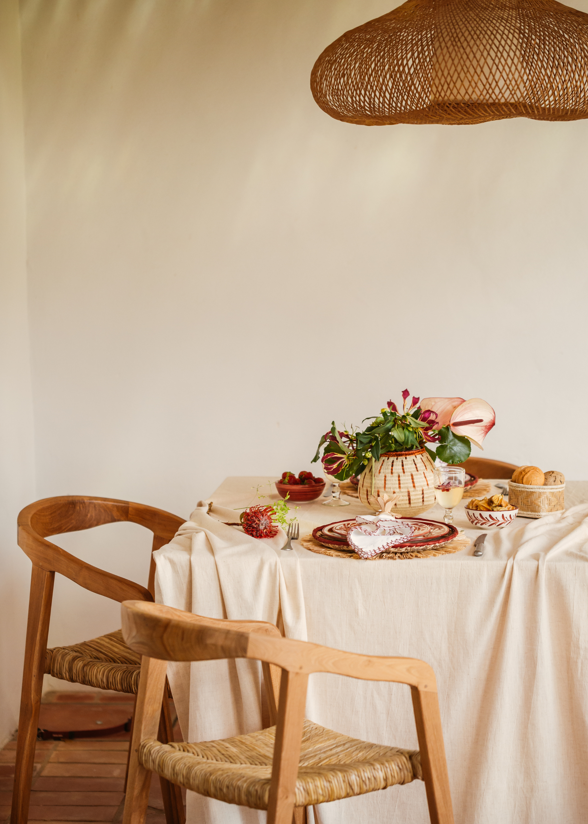 A warm dining space with woven overhead lighting, a set table and food