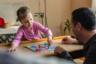 A young girl playing a board game at a table with her dad.