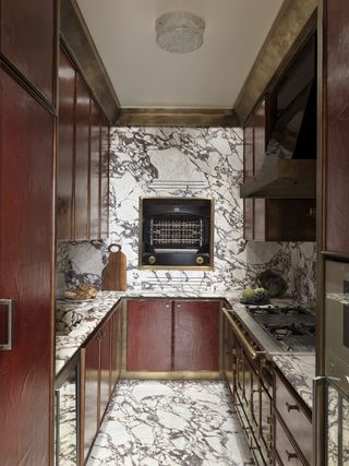 A kitchen with white veined marble, and maroon cabinets