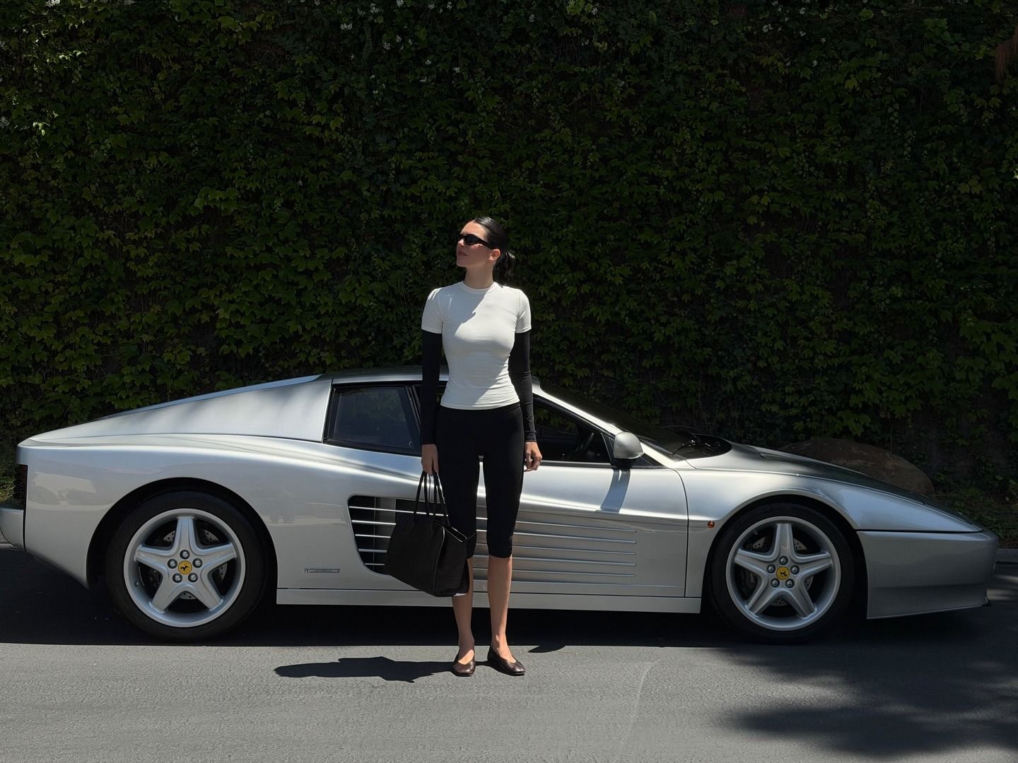 Kendall Jenner posing next to her vintage Ferrari 512 TR sports car wearing an Adanola layered T-shirt and capri leggings with The Row flats.