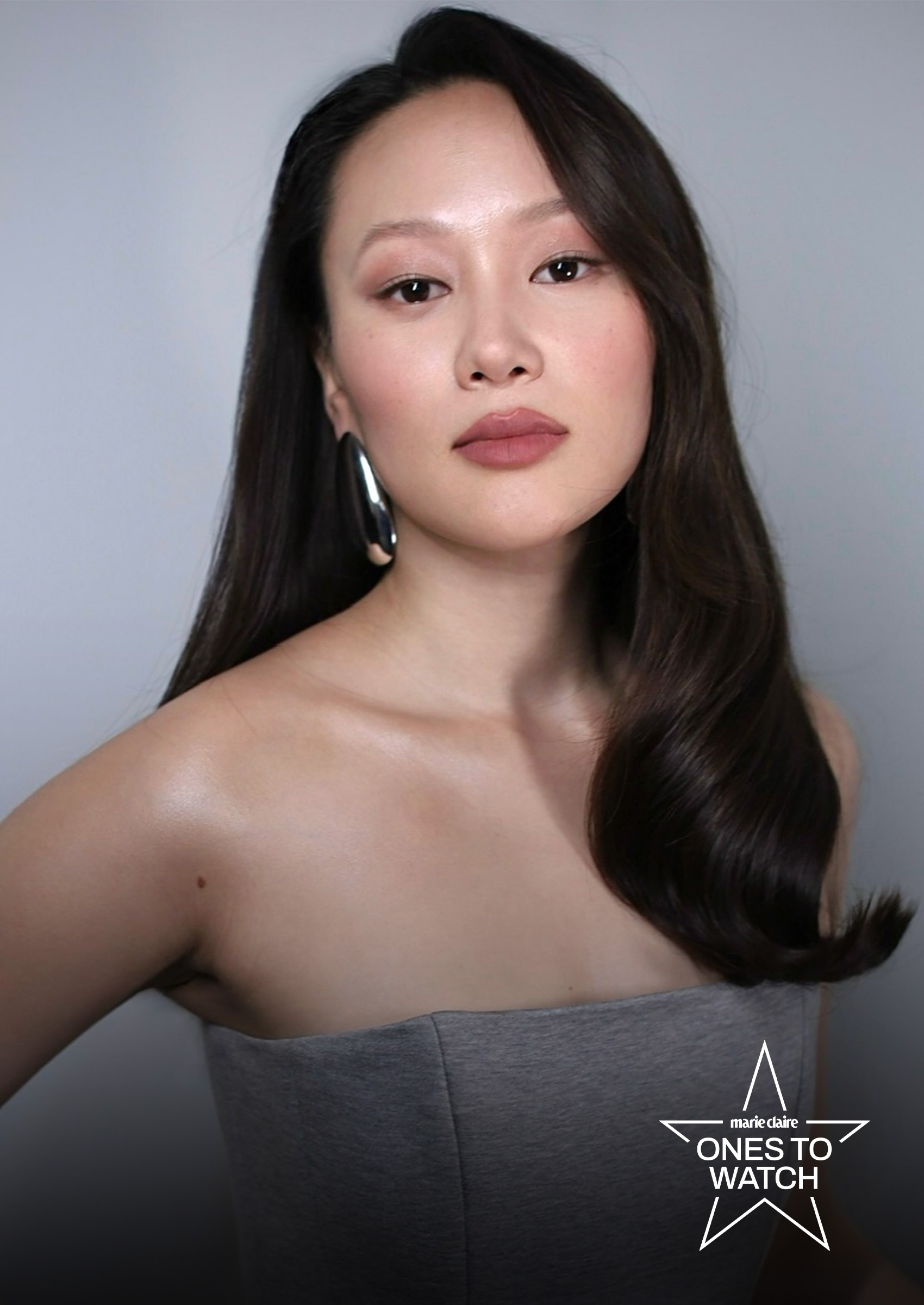 actress yerin ha poses in a grey dress with her hair draped over one shoulder against a grey backdrop