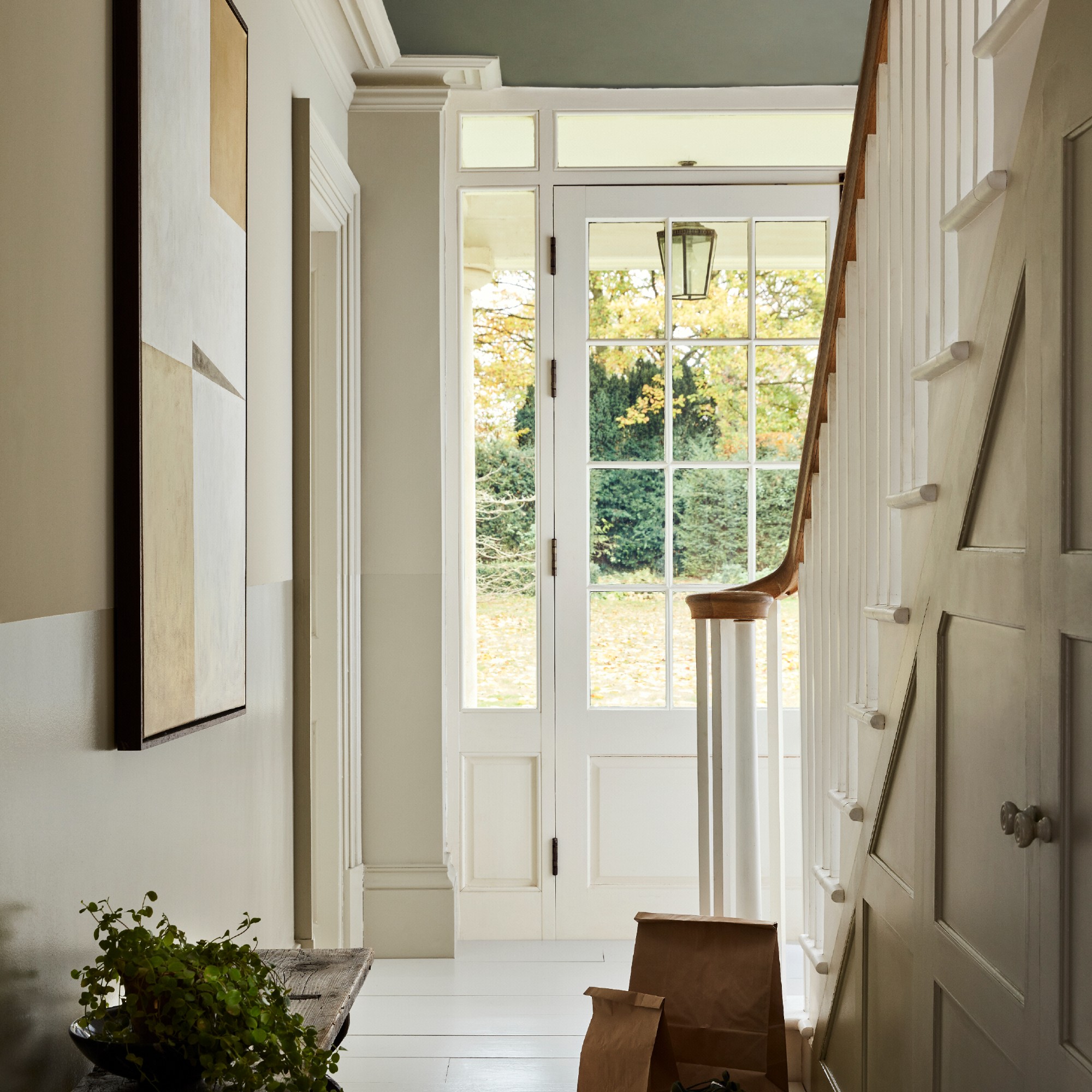 A hallway with a staircase and an abstract painting on the wall painted in Little Greene&#039;s Portland Stone neutral shade