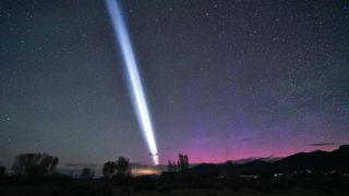 A white streak of light in the night sky with purple auroras visible in the background