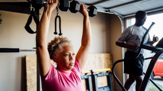 Woman holding two dumbbells above her head in a shoulder press, part of strength training for women