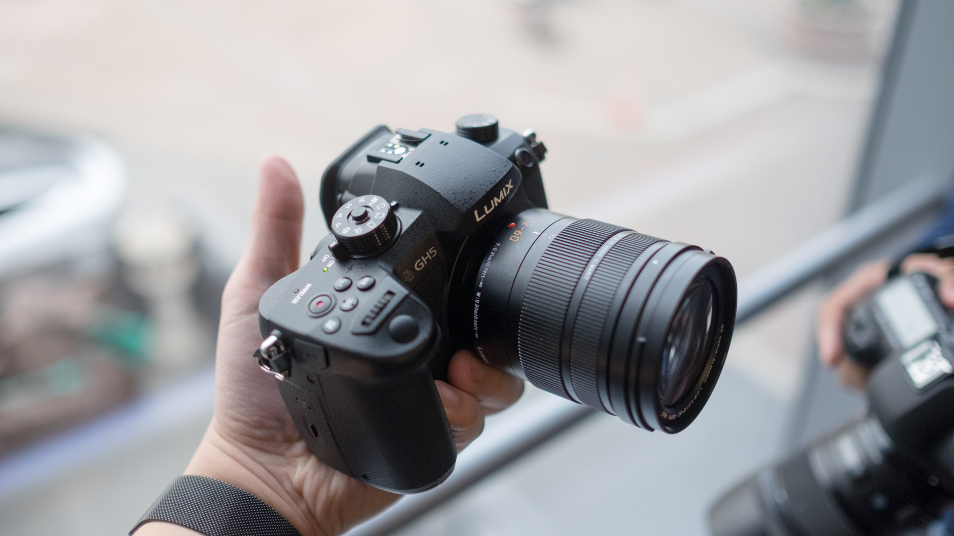 En hand som håller upp en Panasonic Lumix GH5 framför ett fönster.