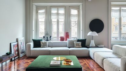 White living room with polished wood floor, white modular corner sofa and green velvet upholstered coffee table