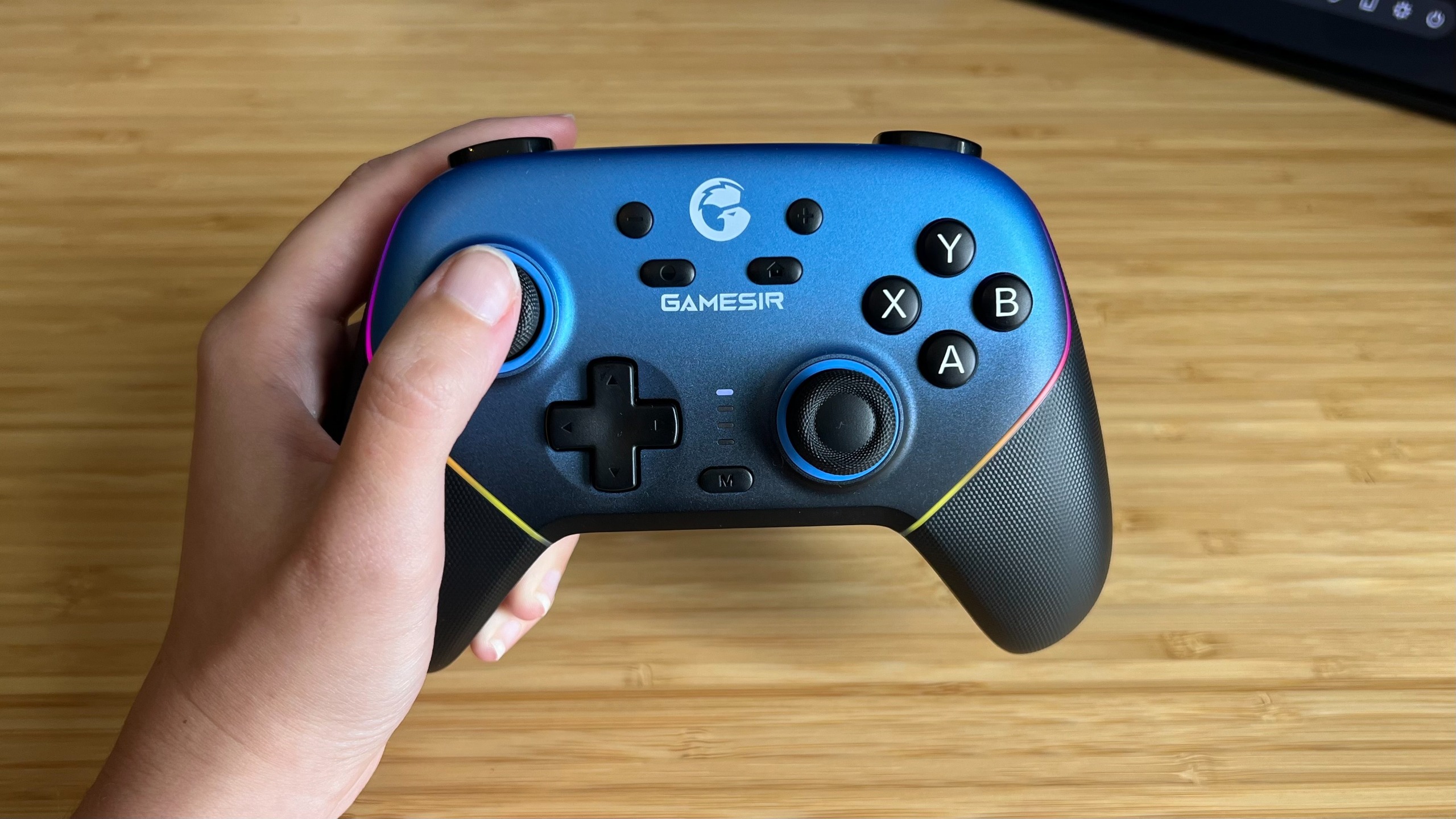 Hand holding GameSir Super Nova controller over a wooden desk