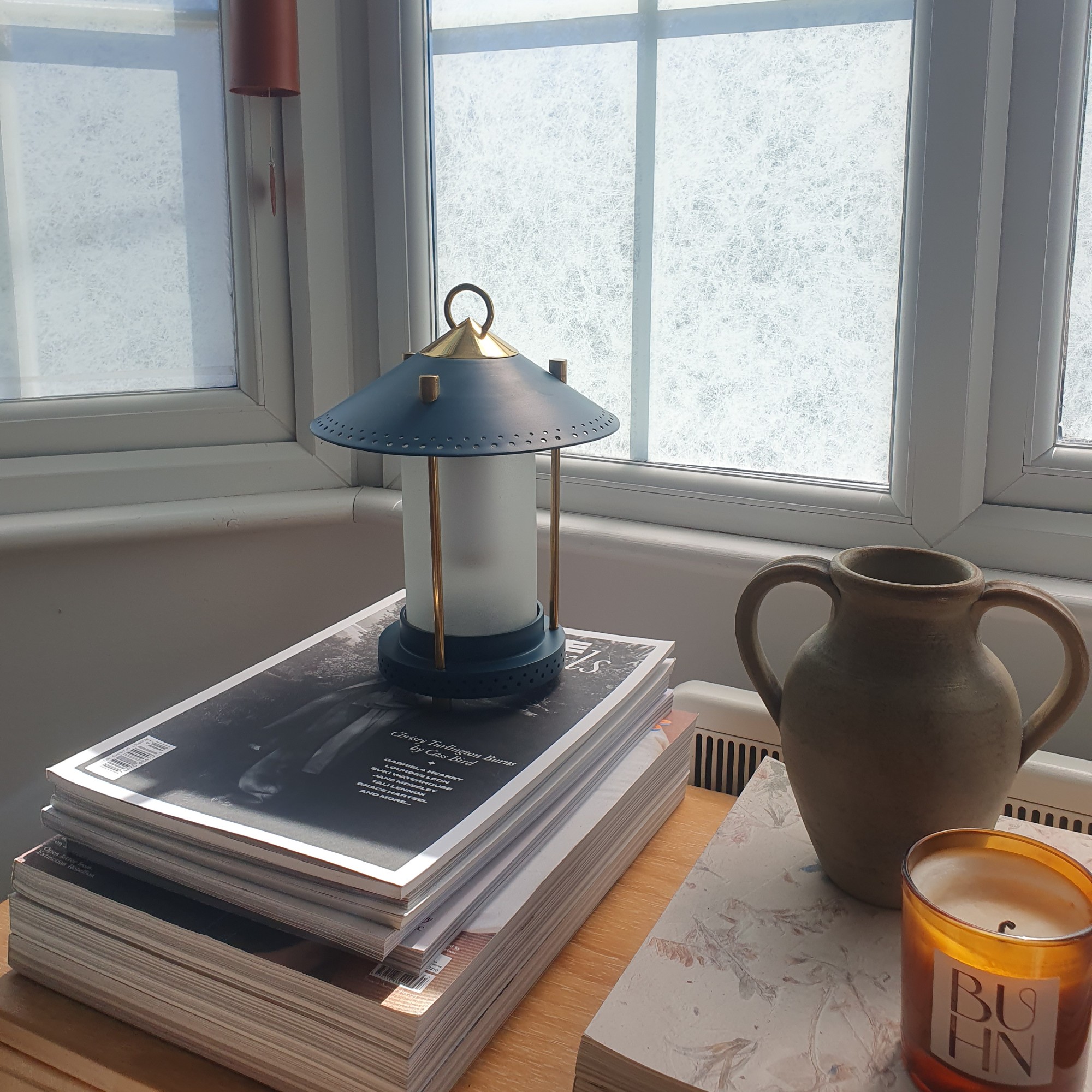 The Pooky Stefan smaller rechargeable lantern in denim on a sideboard on top of a stack of magazines