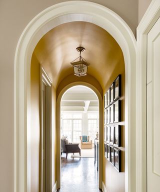 A yellow painted small hallway idea with archway through to the living room and gallery wall.
