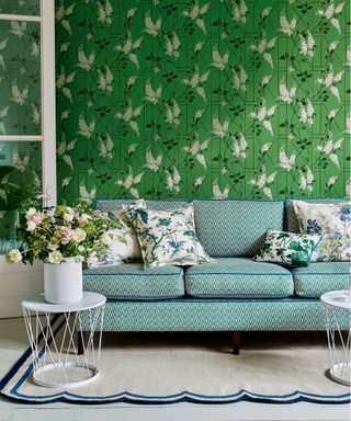A bright green floral and geometric patterned wallpaper behind a blue sofa and neutral accessories.