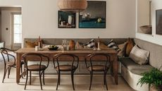 a large banquette dining nook in an English country home with upholstered storage bench seat, rustic wooden table and vintage chairs