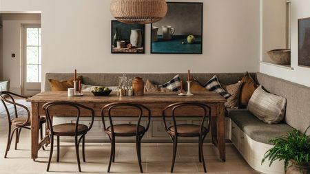 a large banquette dining nook in an English country home with upholstered storage bench seat, rustic wooden table and vintage chairs