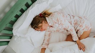 A woman in floral pyjamas sleeping on her side in a cosy bed with the duvet bunched around her legs