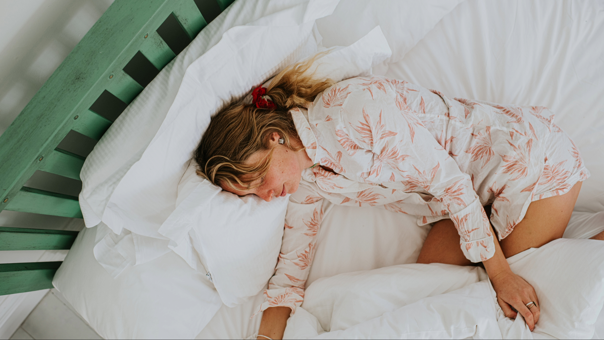 Una mujer en pijama floral durmiendo de lado en una cama acogedora con el edredón enrollado alrededor de sus piernas