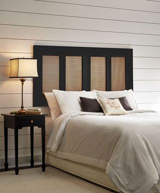 A wood and perforated metal DIY headboard idea in bedroom with cream lampshade and cream shiplap wall decor