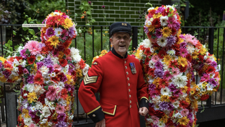 Chelsea pensioner in red coat poses with flower-covered figures at Chelsea Flower Show