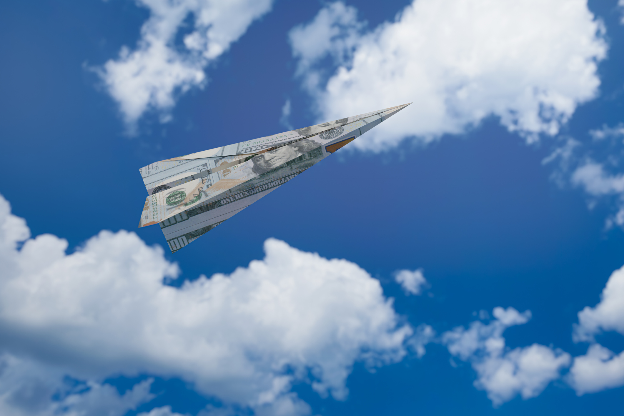paper airplane made of money flying in clouds