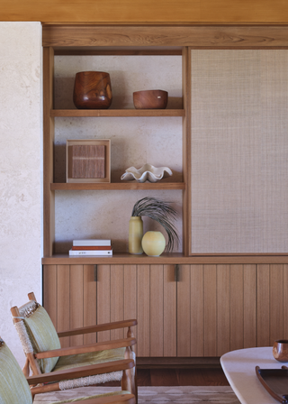 A minimal, earthy living room with shelving featuring wooden bowls, vases and books