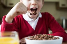 Child in school uniform eating ultra-processed chocolate breakfast cereal