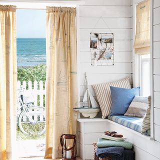 house with white wooden walls and printed curtains near blue sea