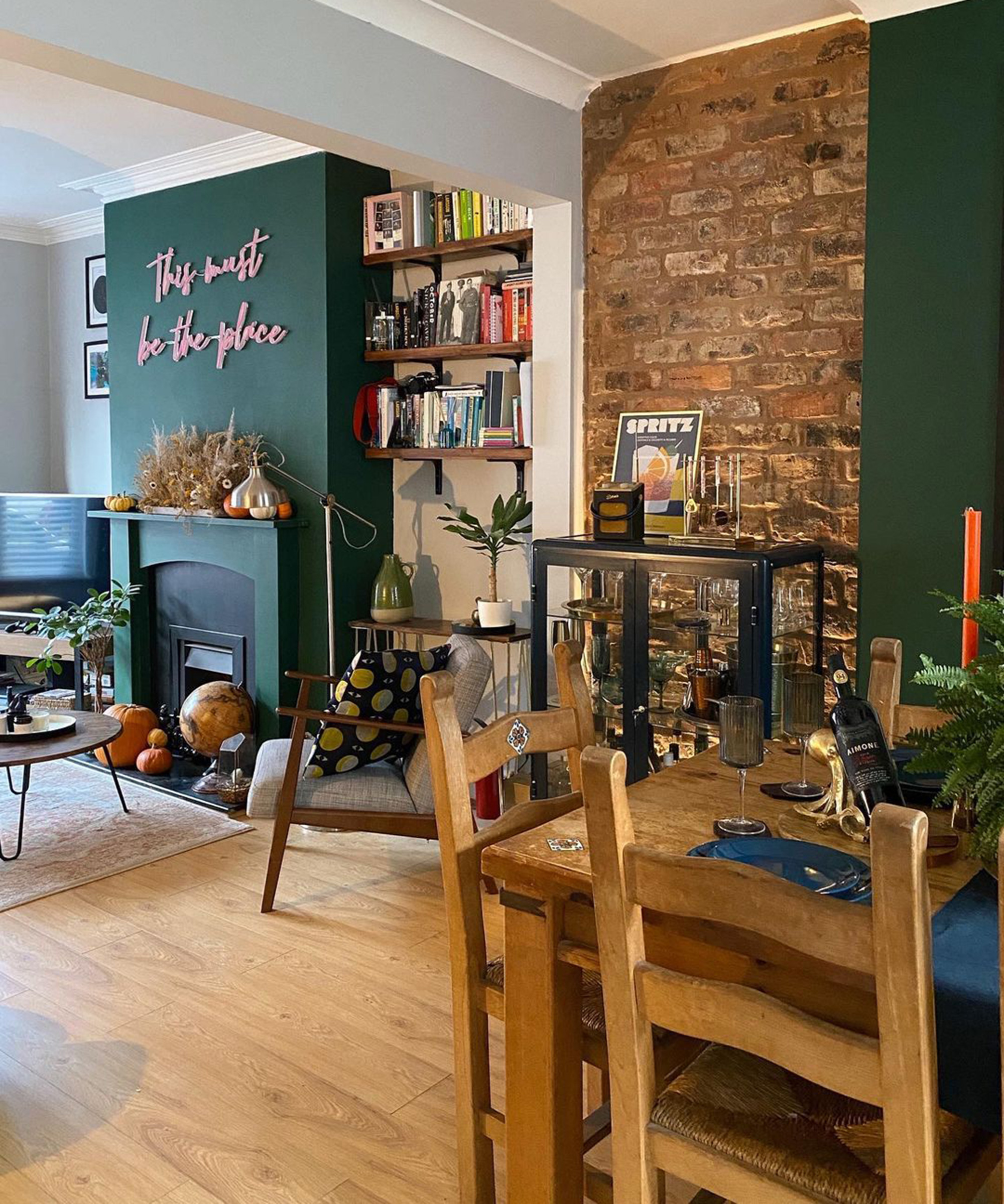 A open-plan living room and diner with green wall decor, bar cart and reading nook