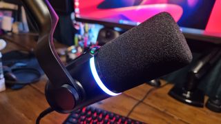 A HyperX FlipCast microphone, lit up in RGB and attached to a boom arm over a gaming keyboard