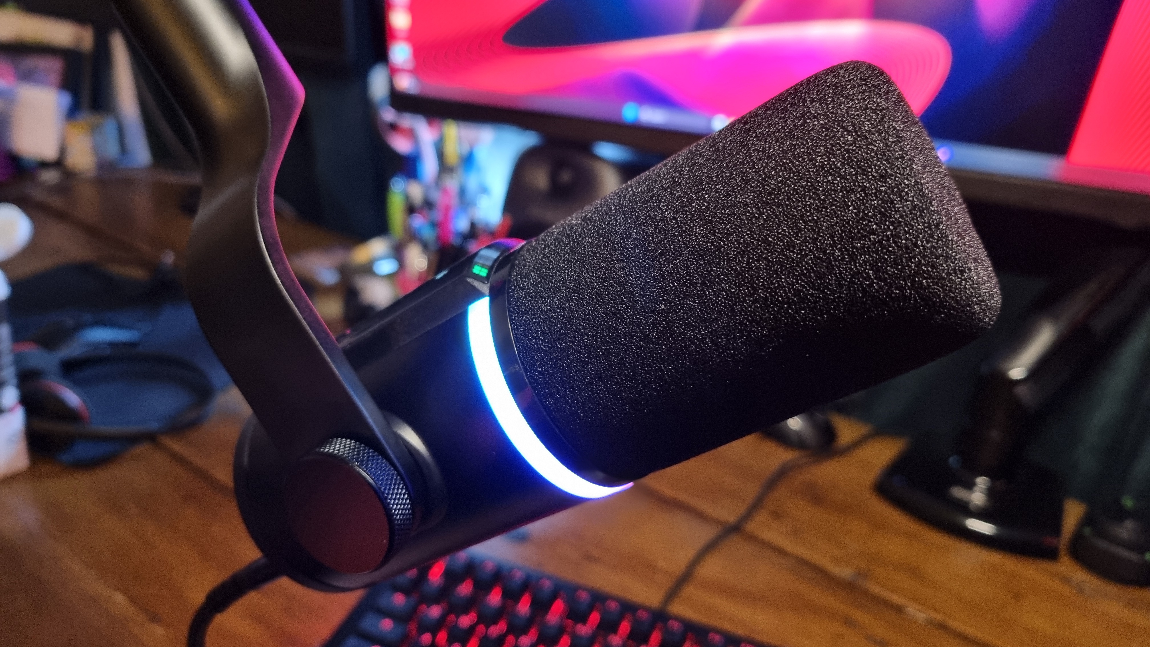 A HyperX FlipCast microphone, lit up in RGB and attached to a boom arm over a gaming keyboard