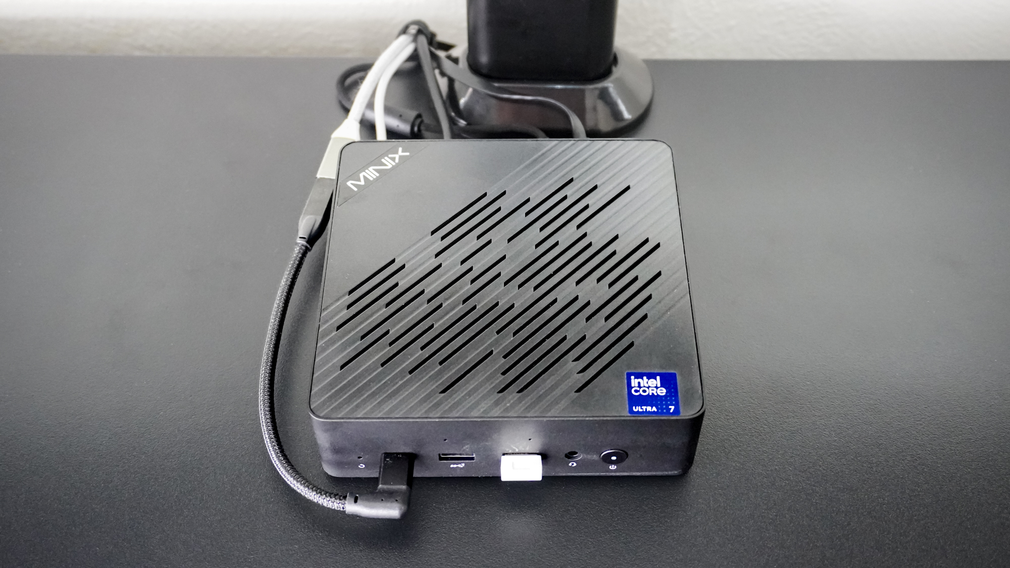 An overhead shot of the Minix Elite EU715-AI on a desk showing a USB-C extension cable connected to the Thunderbolt 4 port on the front