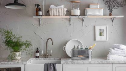a stylish kitchen/utility room with wooden open shelving, grey walls, and a sink on a marble countertop, with a tin of detergent and white towels