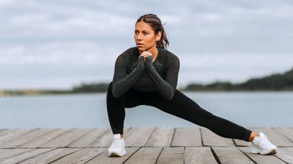 Woman performing a Cossack squat with right knee bent and left knee extended with backdrop of a river 